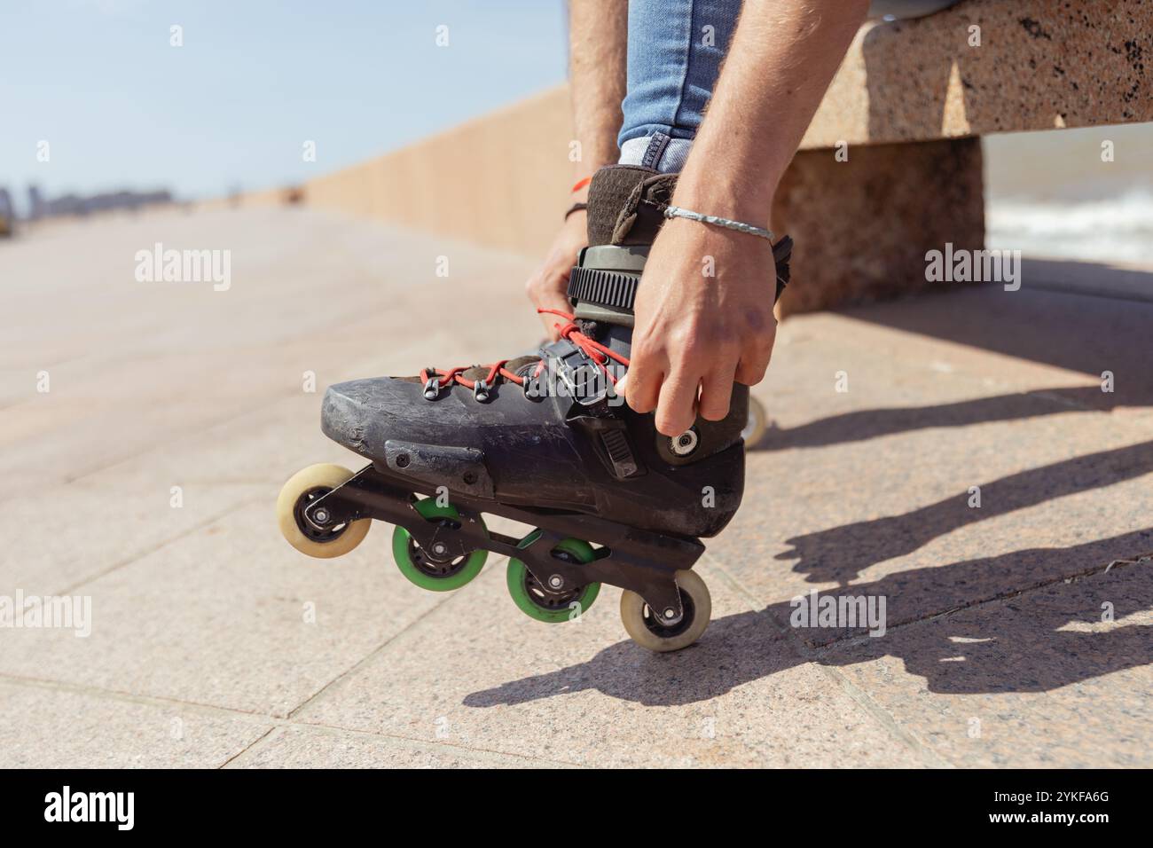Der junge Mann, der Inline-Skates für Inline-Skates anpasst, wird bei sonnigem Wetter im Freien aufgenommen. Stockfoto
