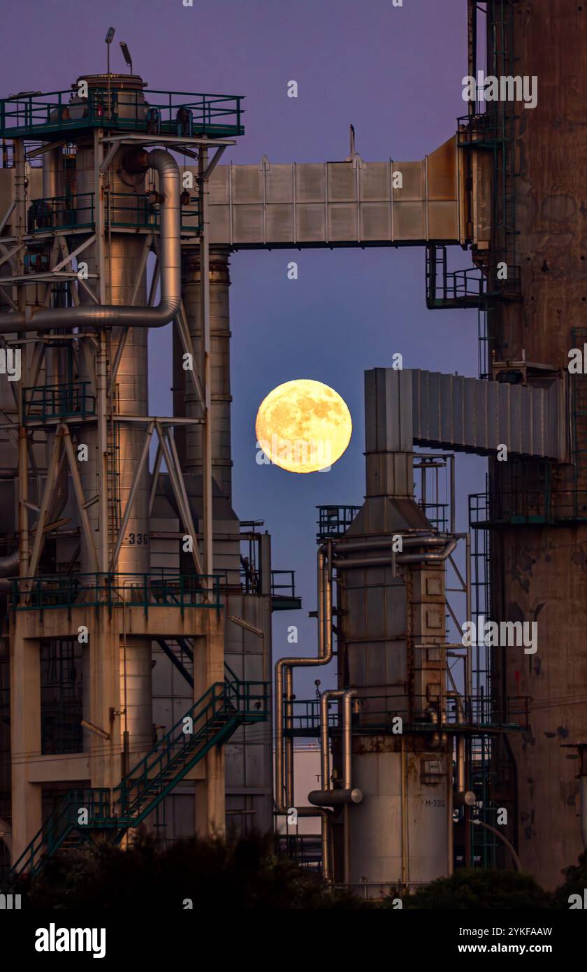 Ein atemberaubender Vollmond steigt am Dämmerungshimmel auf, eingerahmt von den komplizierten Strukturen einer Industrieanlage in Porto, Portugal, und schafft ein Nebeneinander Stockfoto