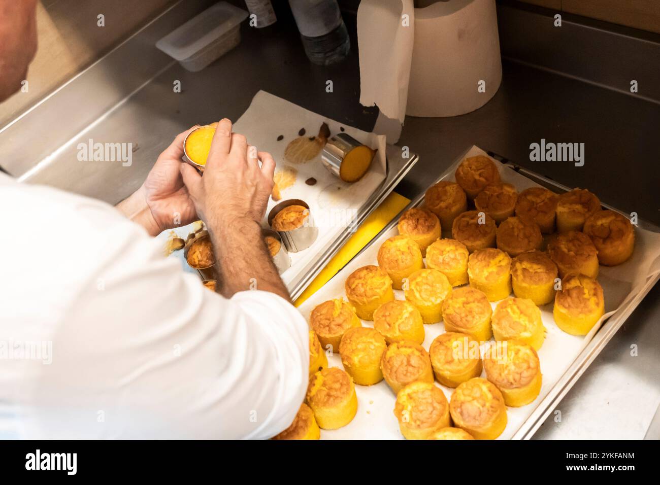 Küchenchef entformt frisch gebackenes Gebäck mit Metallringen in einer Restaurantküche. Das Bild unterstreicht die Präzision und Liebe zum Detail, die in p Stockfoto