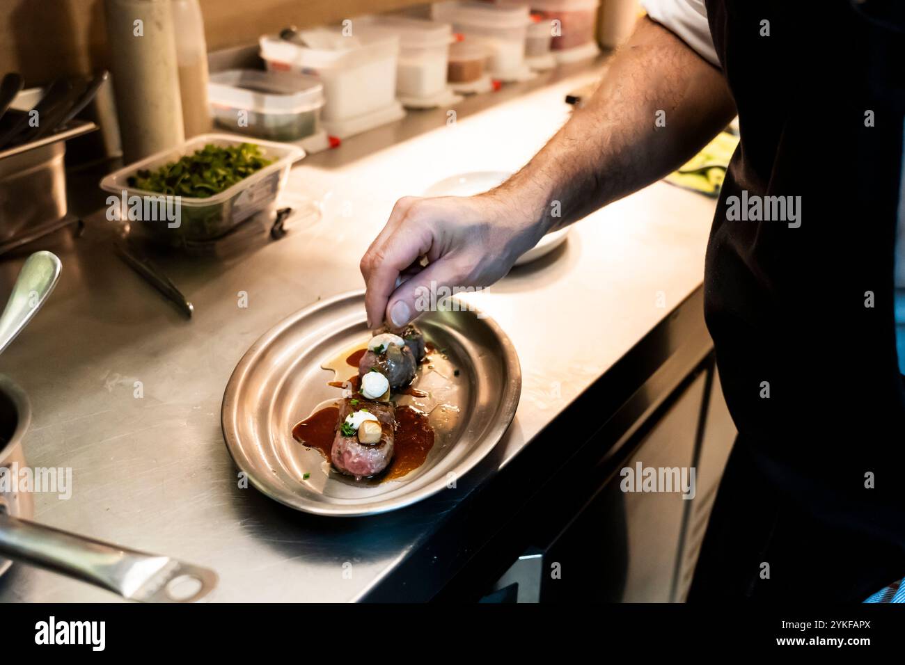 Ein erfahrener Koch in einer geschäftigen Restaurantküche garniert ein Gourmetgericht mit präziser Finesse und Aufmerksamkeit und demonstriert professionelle kulinarische Kunst Stockfoto