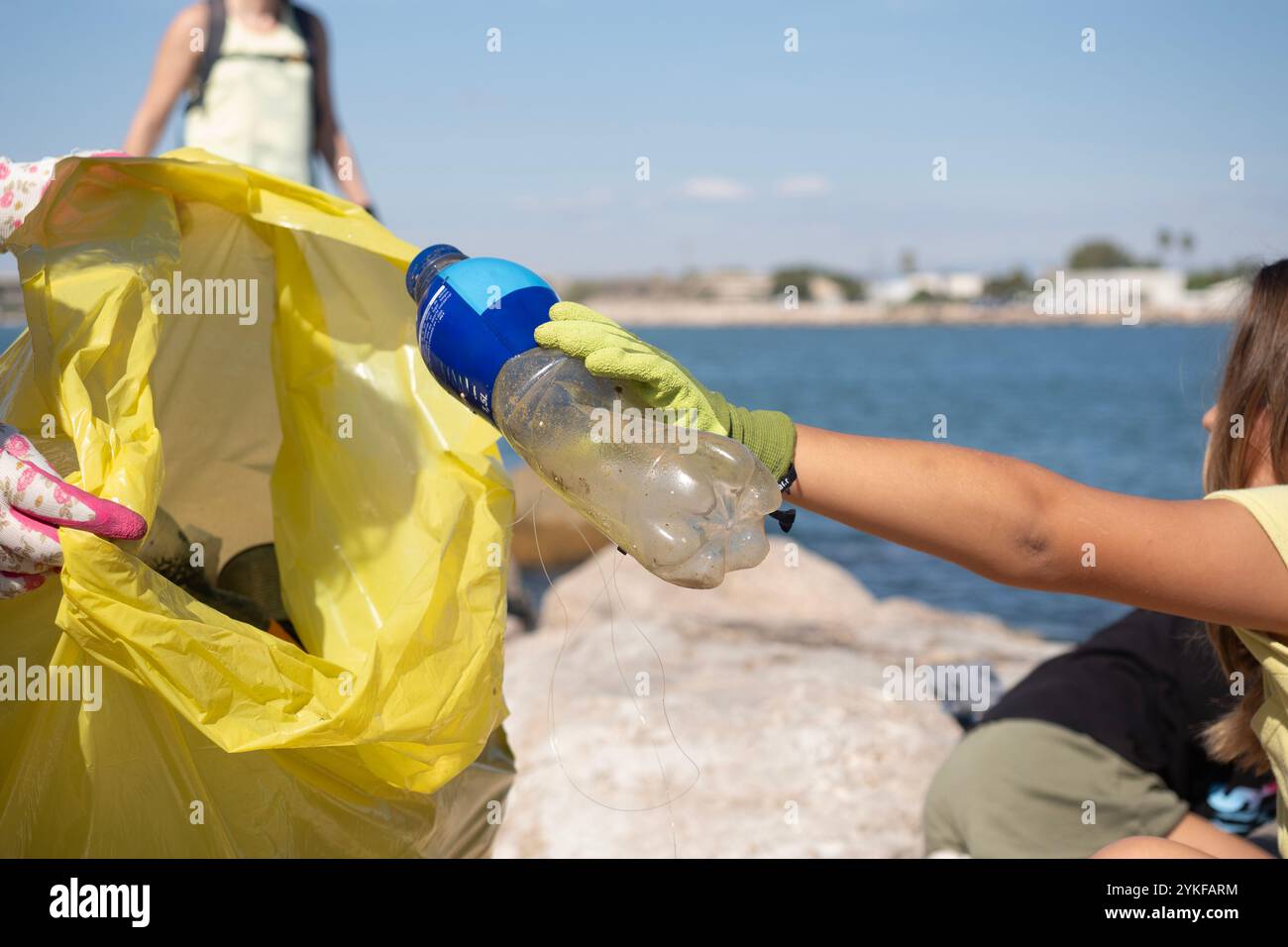 Zwei Freiwillige, die Handschuhe tragen, entfernen Plastikflaschen und Müll aus einem Küstengebiet und zeigen damit Verantwortung für die Umwelt und den Schutz der Meere Stockfoto