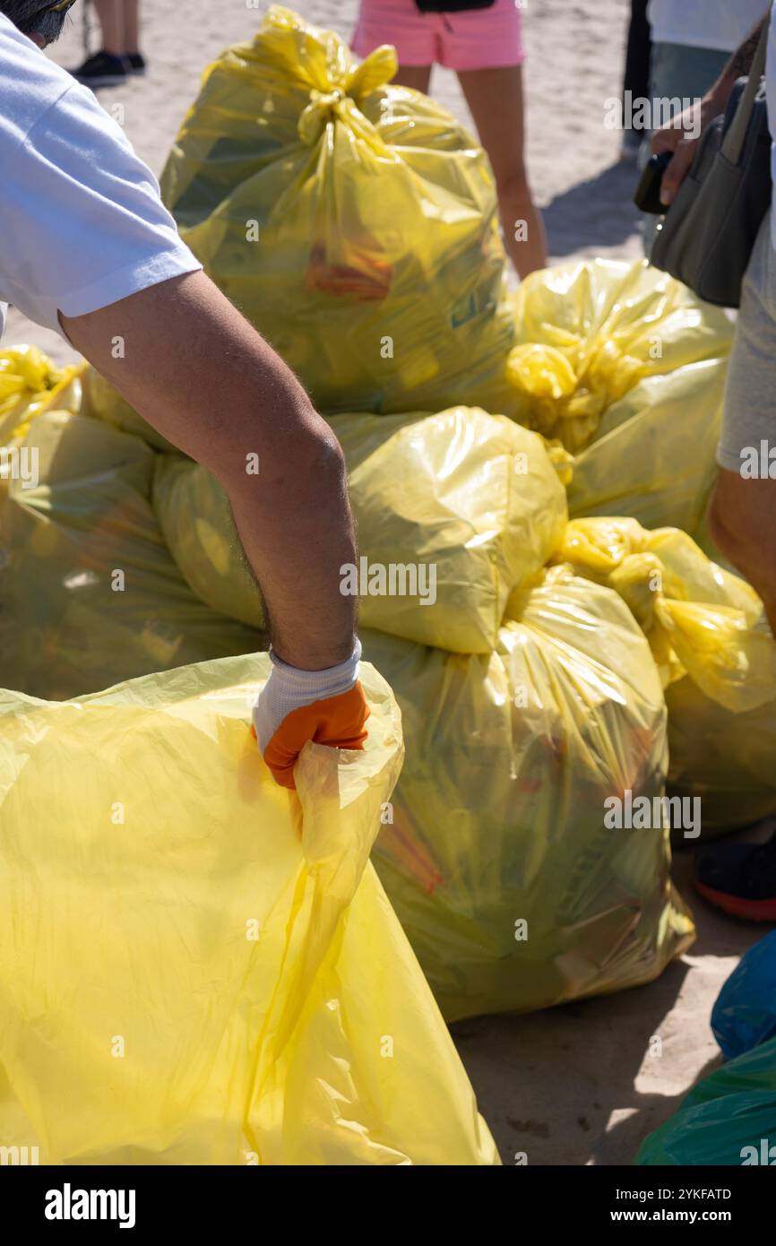 Eine Nahaufnahme von Freiwilligen, die Müll in gelben Plastiktüten sammeln, um einen Sandstrand zu reinigen, um Umwelt- und Meeresschutz zu fördern Stockfoto
