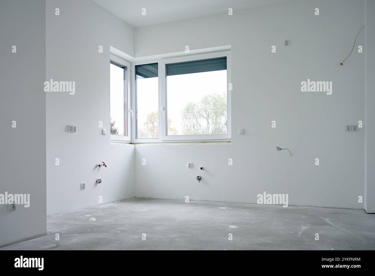 Geräumiges leeres Apartment, das renoviert wird, mit großem Fenster, Betonboden und weißen Wänden. Neubau im Bau Stockfoto