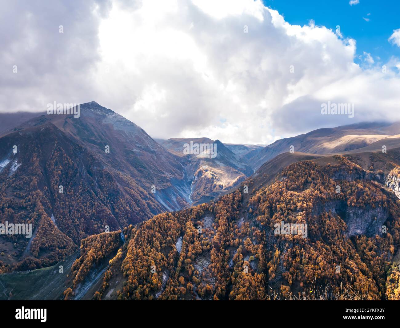 Herbstlich gelbe braune Bäume auf vielen komplexen Felshügeln und Bergen auf weißem Wolkengrund und blauem Himmel, Blick auf Georgia Country. Goldenes Moun Stockfoto