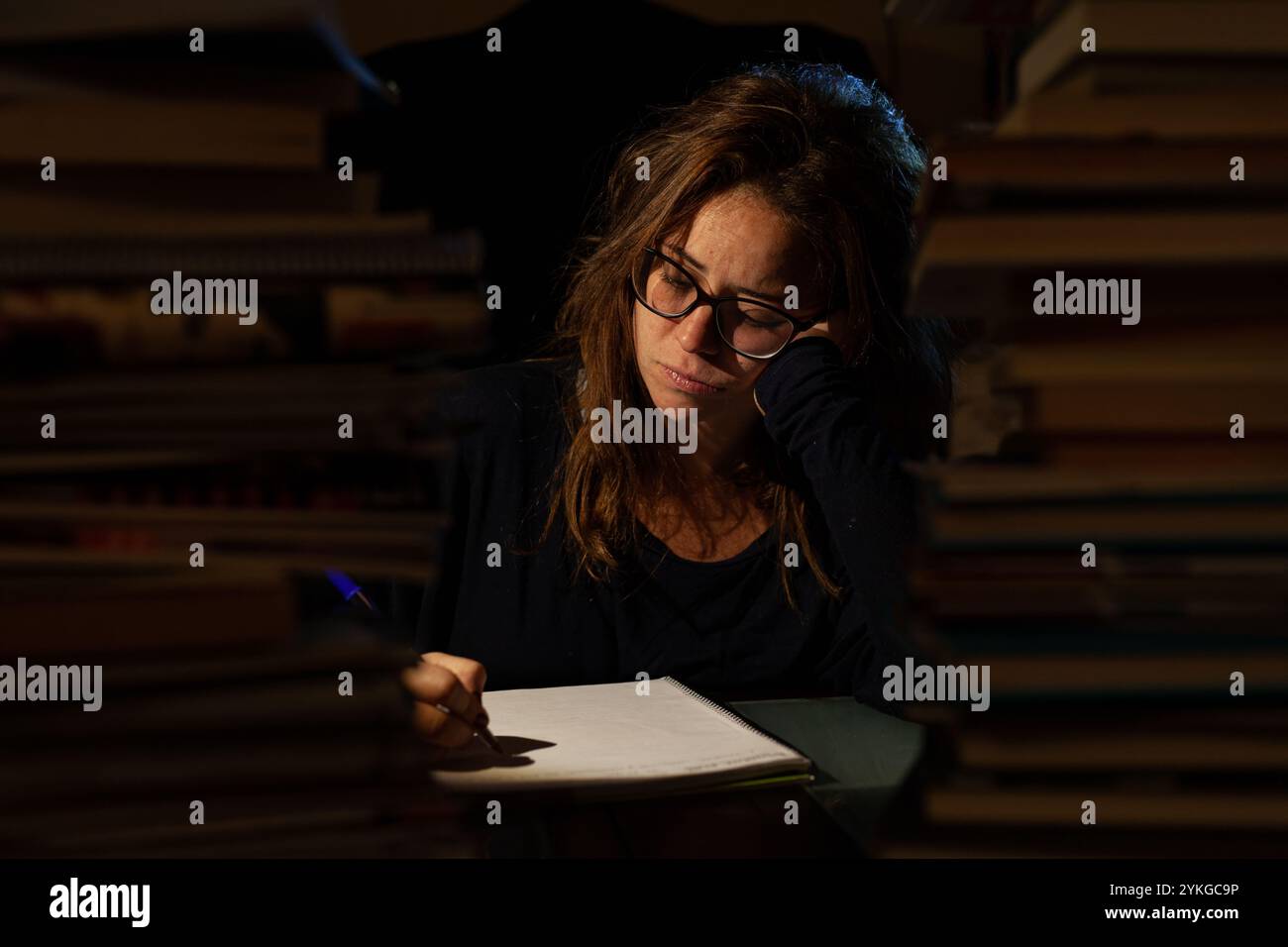 Fokussierter junger Schüler mit Brille, der nachts in einer Bibliothek für Prüfungen studiert Stockfoto