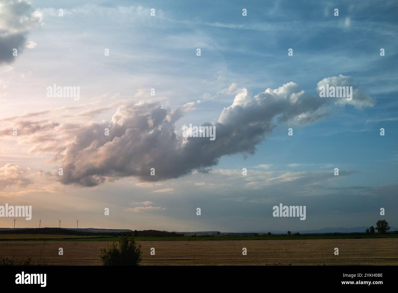 Eine atemberaubende Sturmwolke schwimmt bei Sonnenuntergang ätherisch am Himmel. Es ist eine Panorama-Landschaft mit einigen Windgeneratoren in der Ferne. Konz Stockfoto