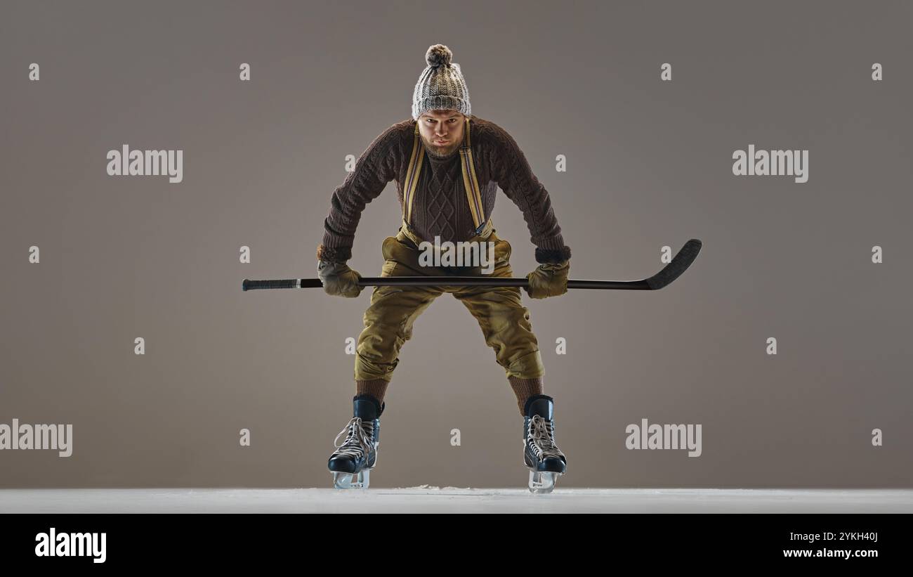 Fokussierter, kompetitiver Mann in Vintage-Kleidung, Pullover, Hut und Hosen mit Hosenträgern, Hockey spielen, Fähigkeiten zeigen Stockfoto