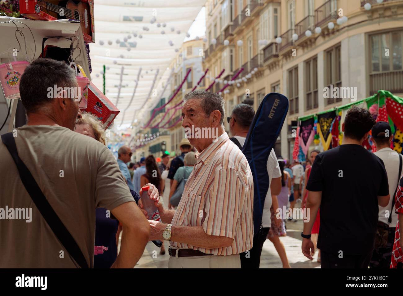 Ein ortsansässiger Musiker mit einer Gitarre auf dem Rücken führt während der lebhaften Málaga August Messe Gespräche Stockfoto