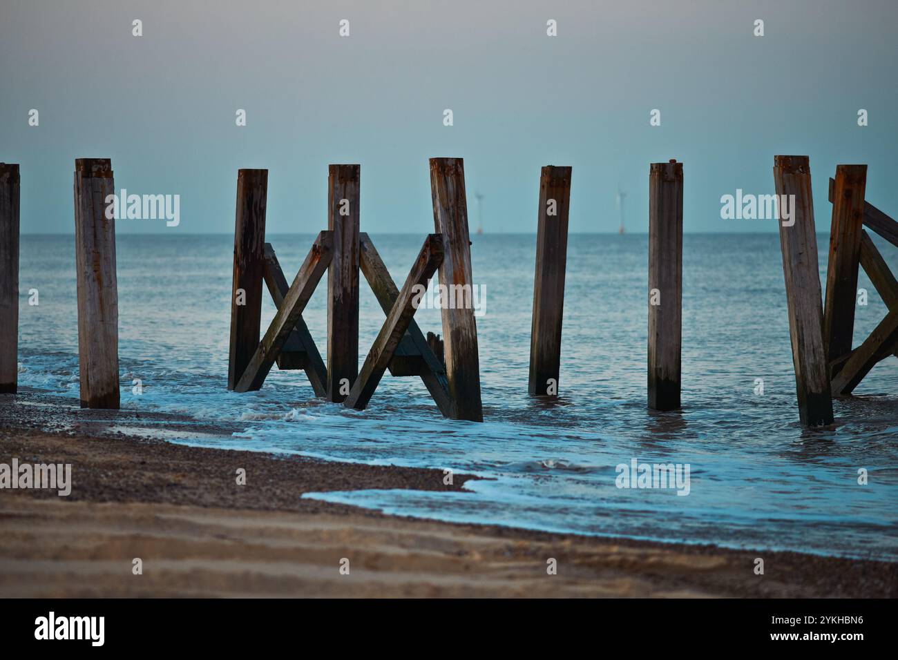 Sonnenuntergang über einem alten Pier am Strand mit Windpark im Hintergrund. Stockfoto