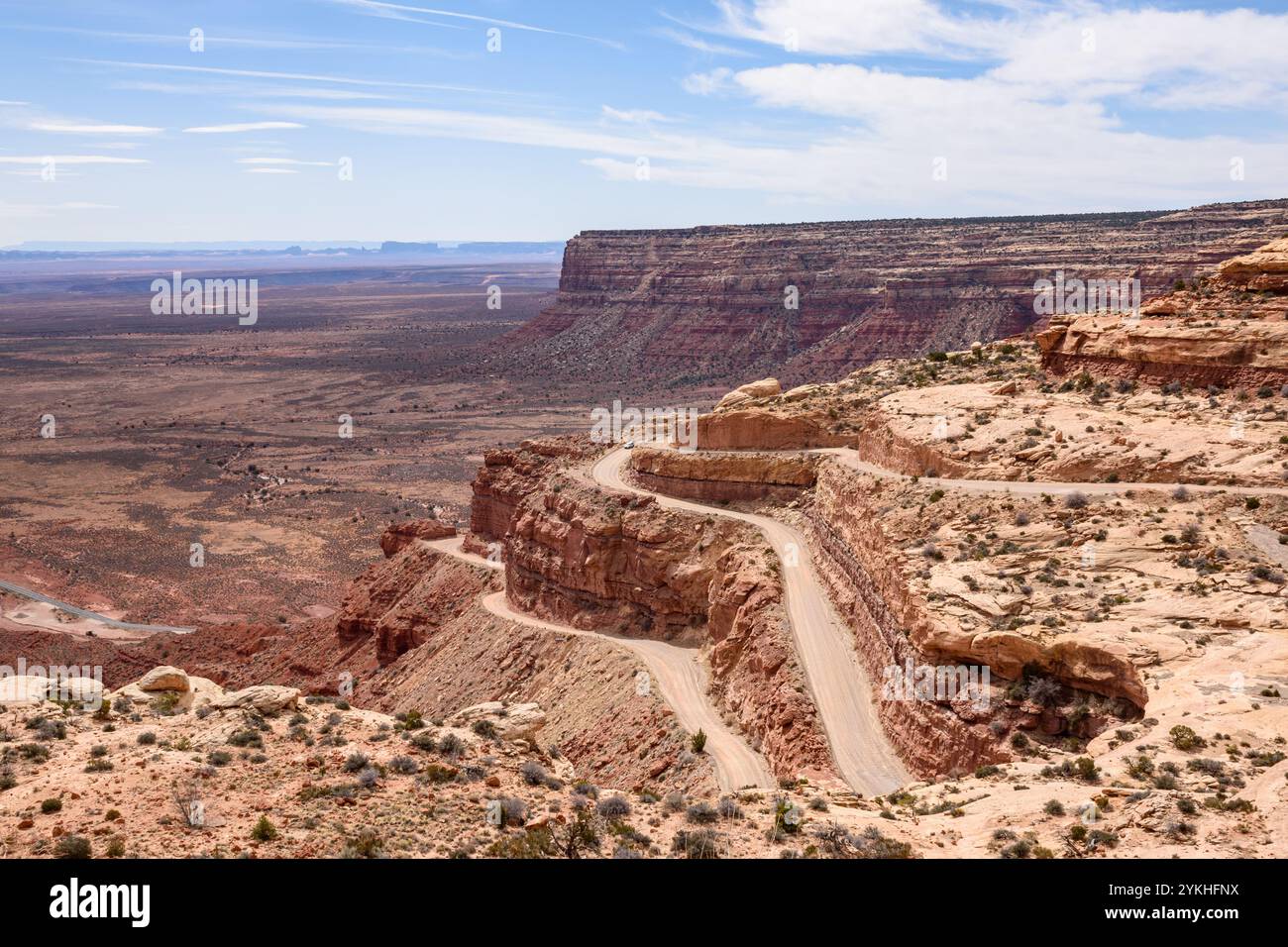 Wunderschöner Panoramablick auf die gewundene und steile Moki Dugway Road in Utah, USA. Die Landschaft zeigt rote Felsformationen und ein Auto, das die Straße überquert. Stockfoto