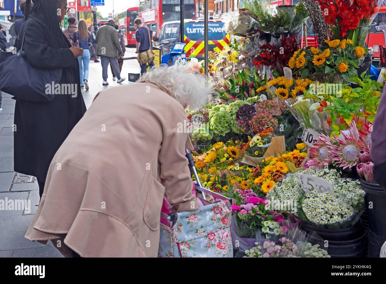 Ältere Frau mit Einkaufswagen, die Blumen am Blumenstand vor der U-Bahn-Station Brixton High Street kauft Oktober 2024 London England Großbritannien KATHY DEWITT Stockfoto