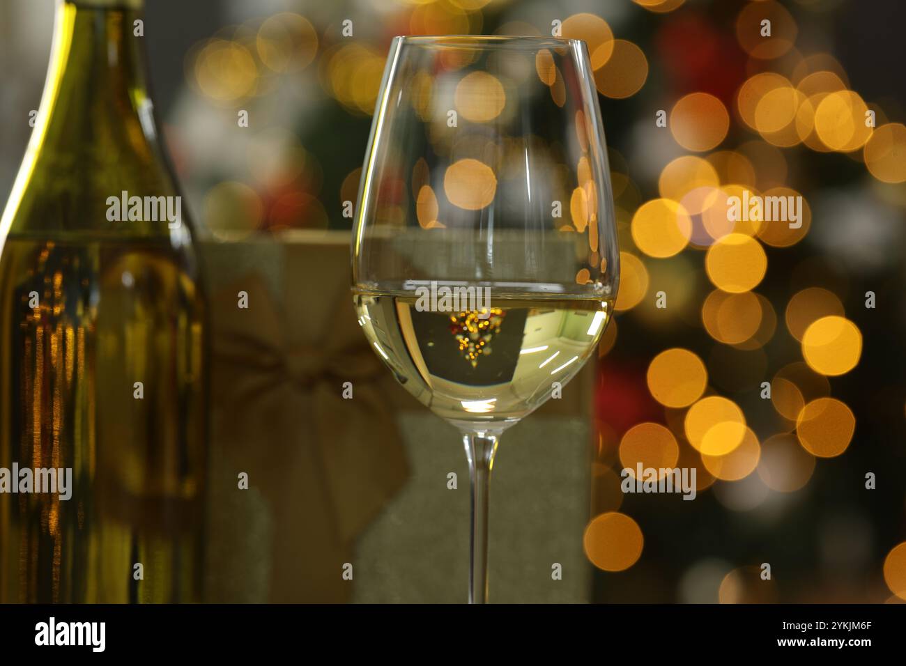 Wein im Glas, Flasche und Weihnachtsgeschenk gegen verschwommenes Licht, Nahaufnahme Stockfoto