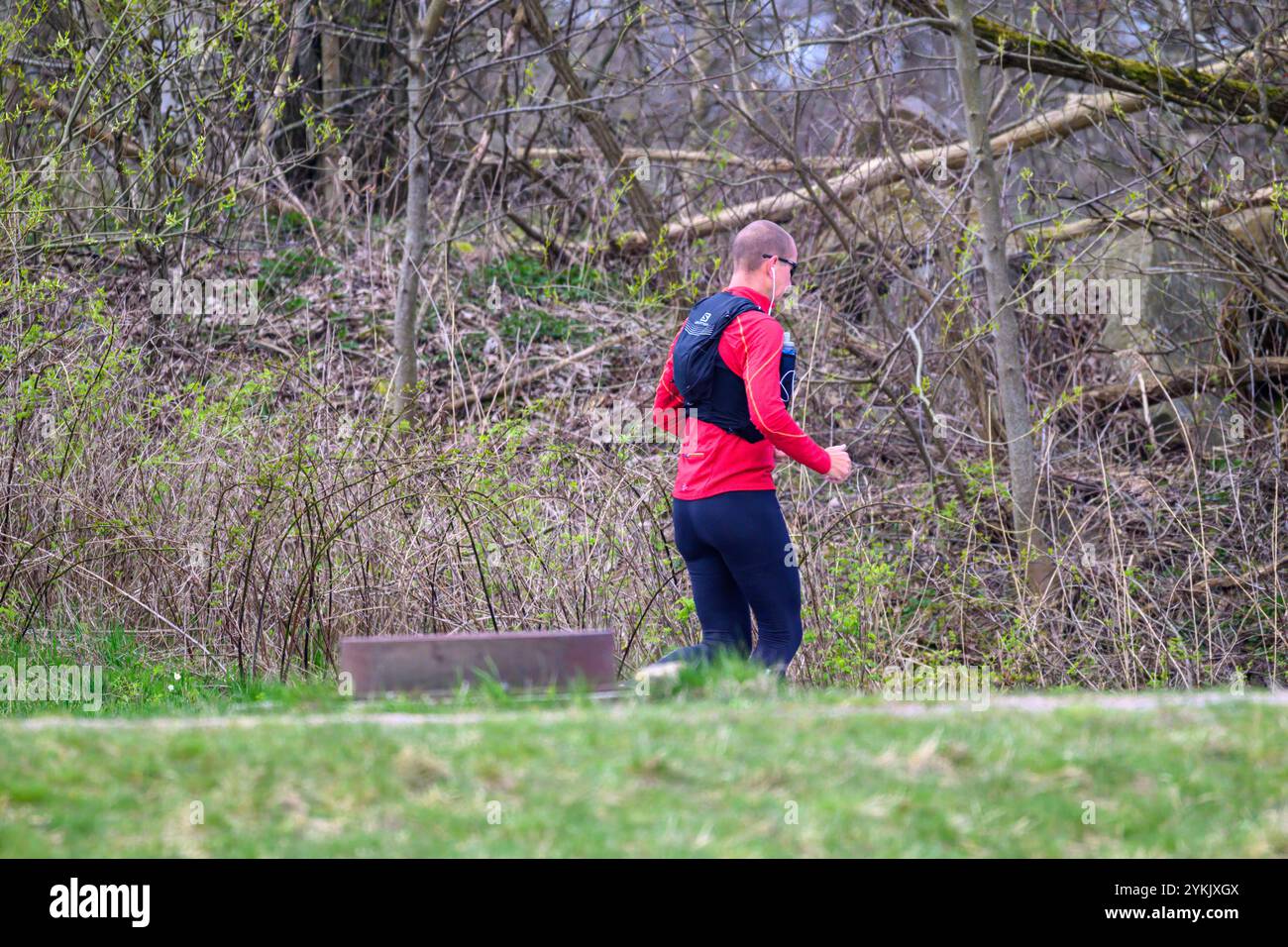 Eine Person joggt auf einem kurvenreichen Pfad in einem Park, mit sportlicher Ausrüstung. Die Umgebung ist mit Büschen und Bäumen geschmückt, was auf eine ruhige Umgebung im Freien hinweist Stockfoto