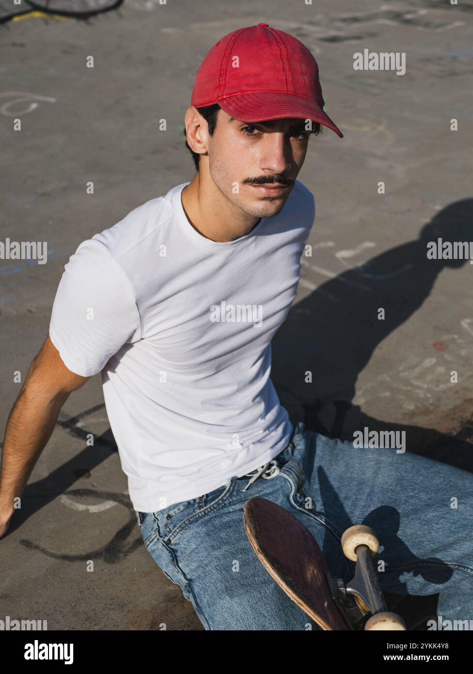 Junger Skateboarder, der sich in einem sonnendurchfluteten urbanen Skatepark entspannt. Stockfoto