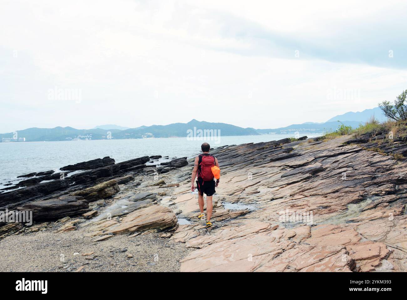 Ein Wanderer, der auf den Sedimentfelsen an der Küste der Insel Tung Ping Chau in Hongkong spaziert. Stockfoto
