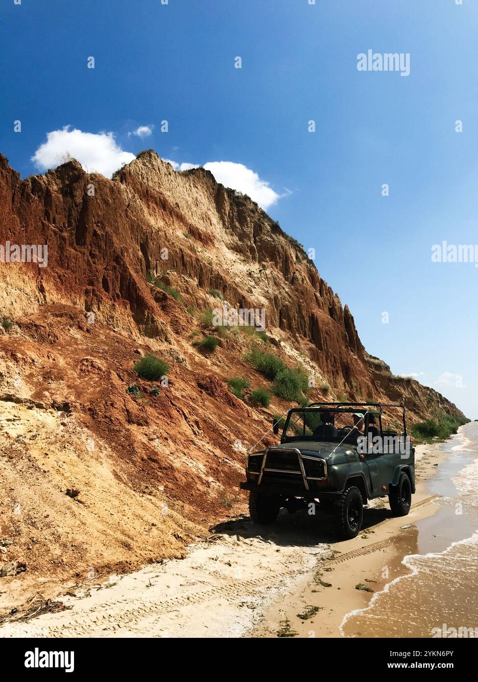 Ein Geländewagen fährt entlang eines abgelegenen Strandes mit zerklüfteten Klippen in der Nähe unter klarem blauem Himmel. Perfekte Darstellung des Abenteuers, nat Stockfoto