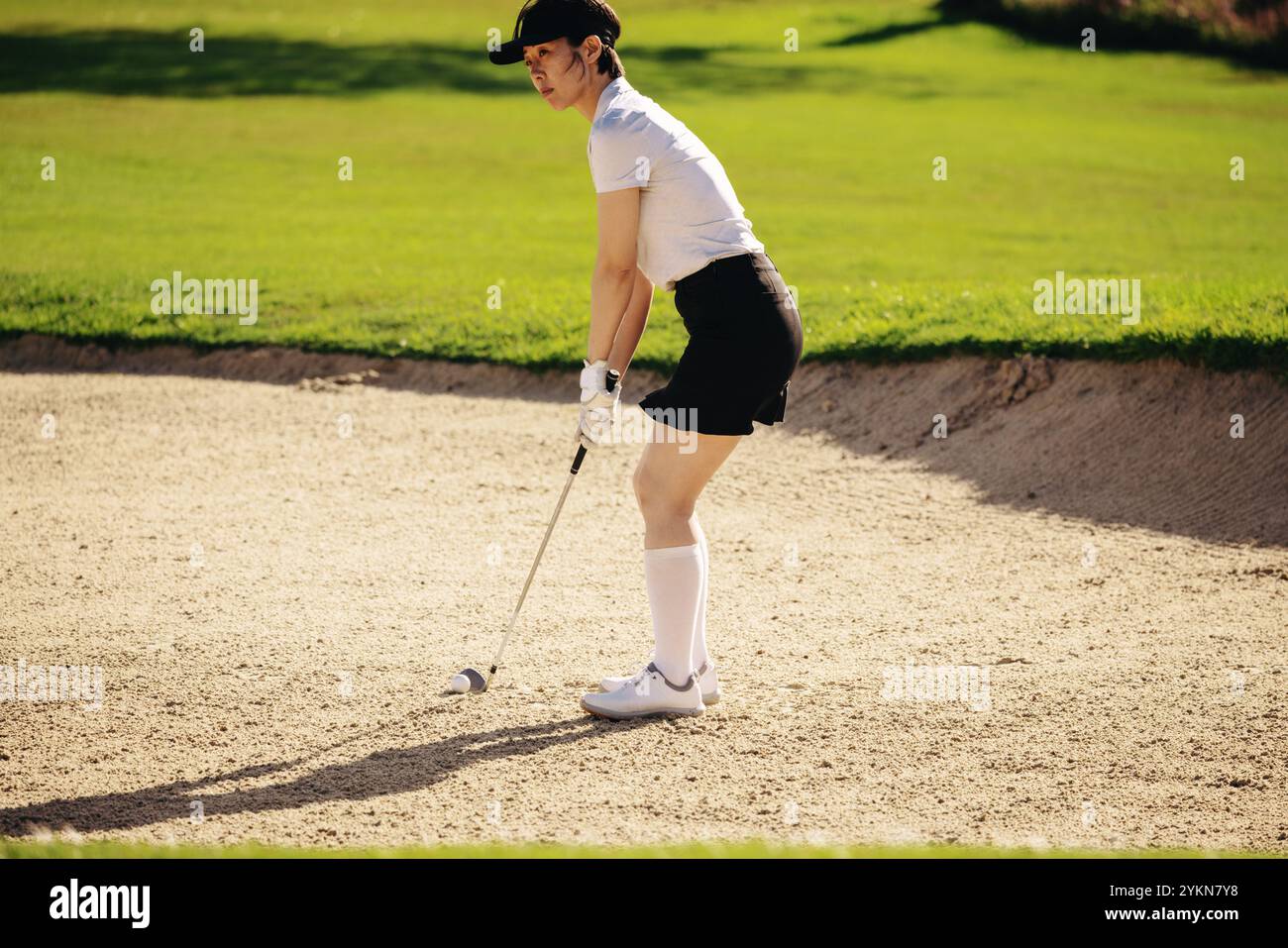 Profi-Golferin in entschlossener Haltung, bereit, an einem sonnigen Tag einen Schuss aus dem Sandbunker mit einem Keileisen zu schießen. Stockfoto