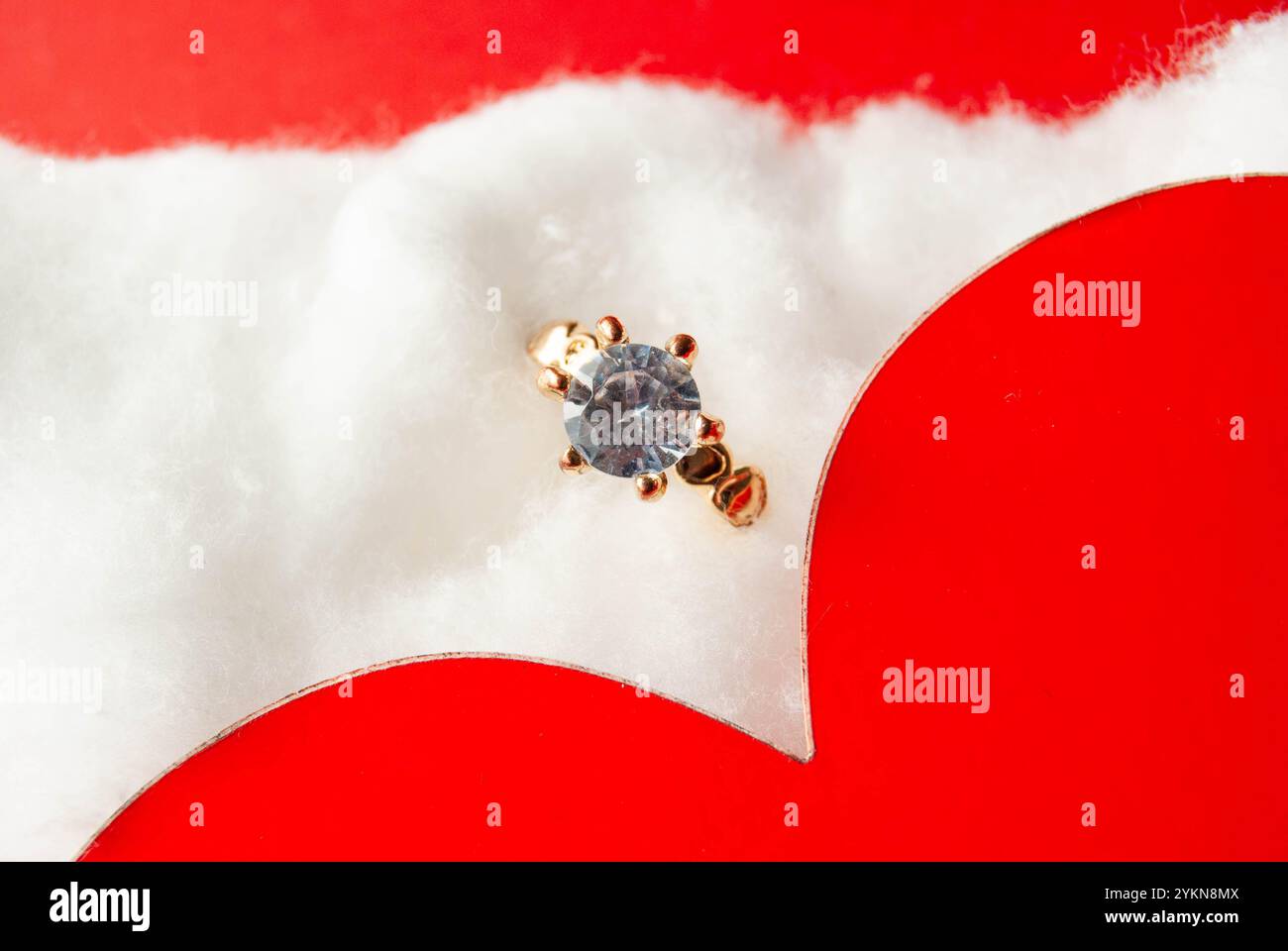 Elegantes Design für den Valentinstag mit rotem Herz, Ring und Baumwollwolle, das Liebe und besondere Momente festhält. Stockfoto