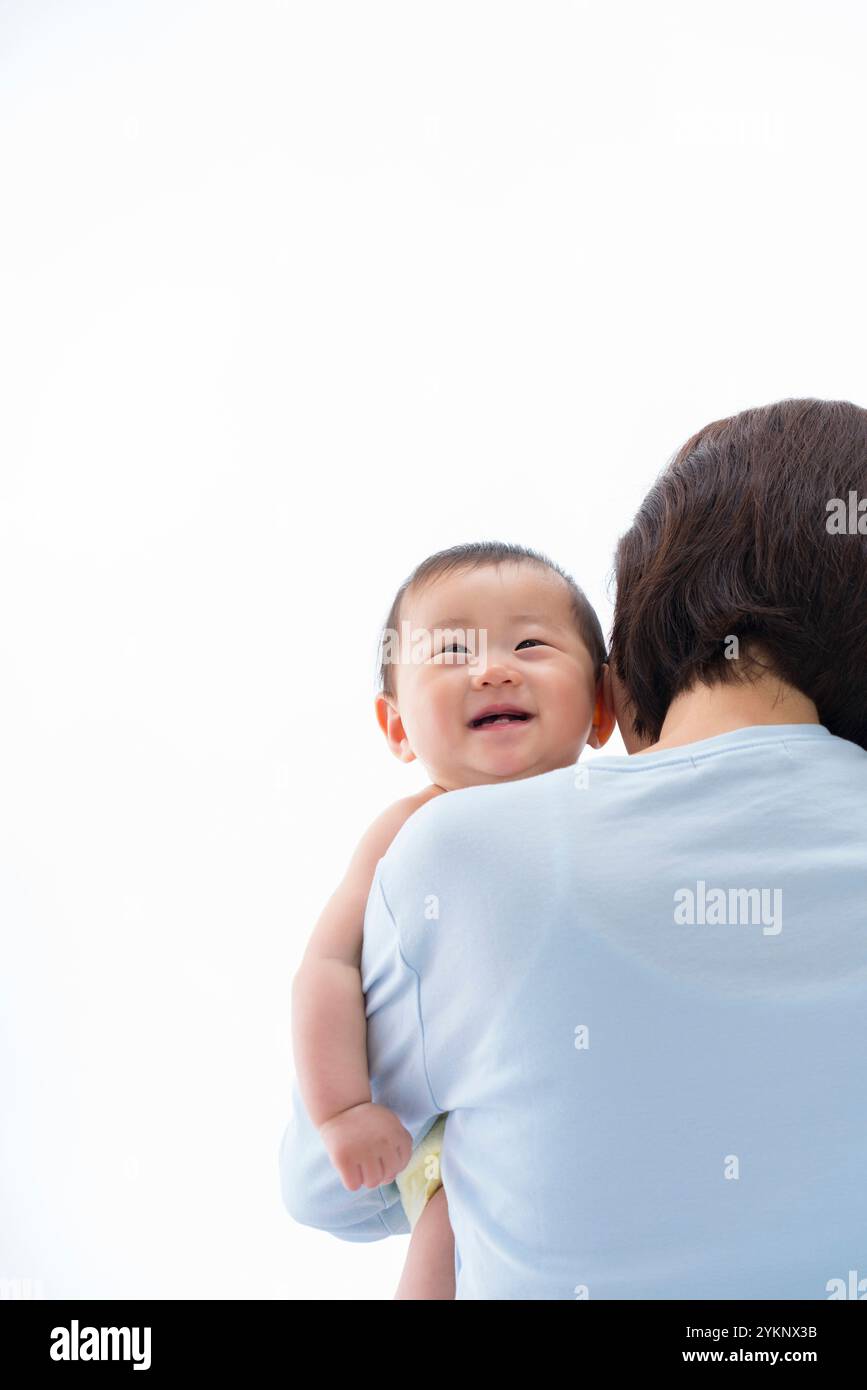 Das Baby lächelt über Mutters Schulter. Stockfoto