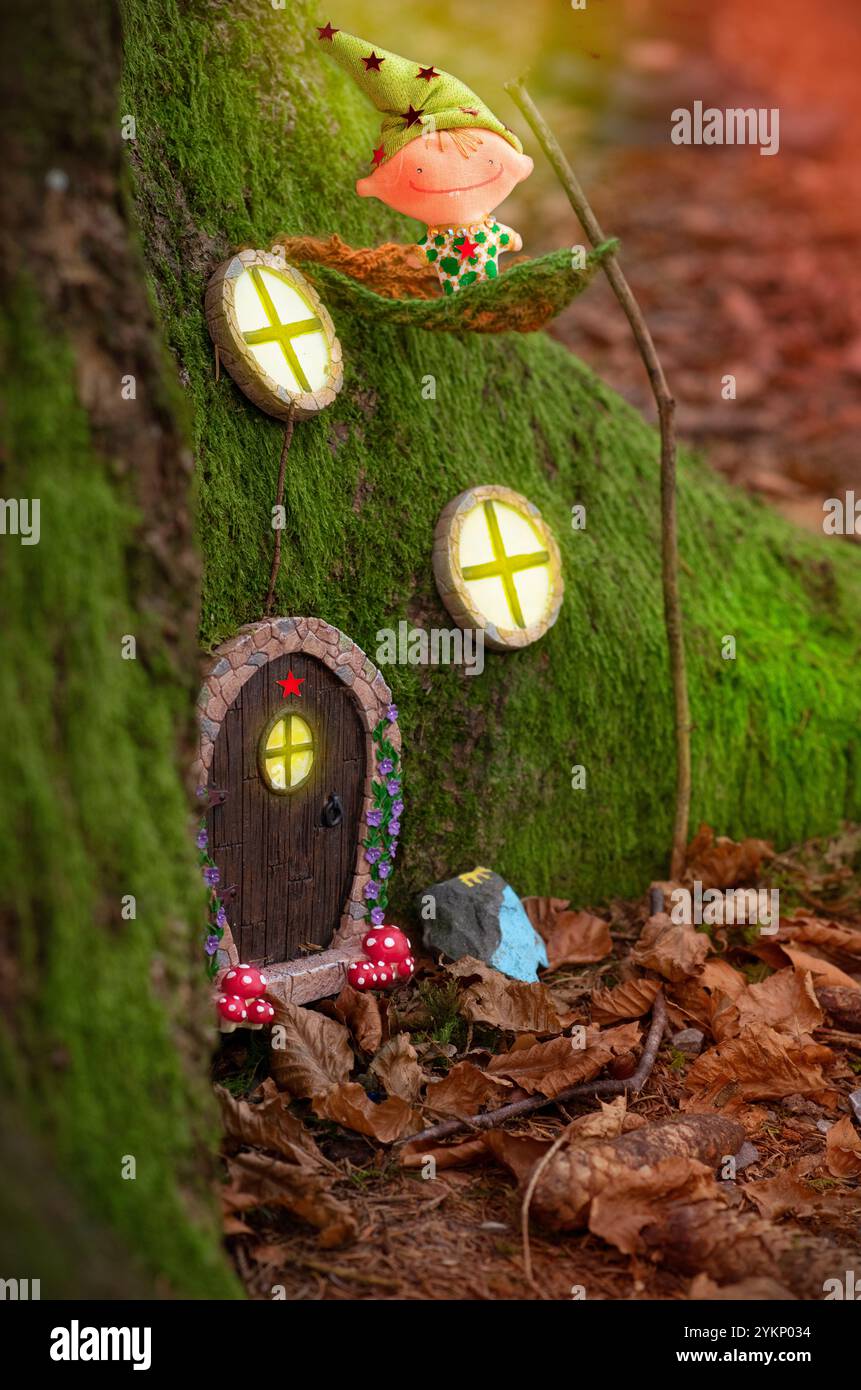 Ein bezauberndes Märchenhaus, eingebettet in die moosigen Wurzeln eines Baumes in einem Wald, mit einer kleinen skurrilen Tür mit einem roten Stern, umgeben von winzigen Fenstern Stockfoto