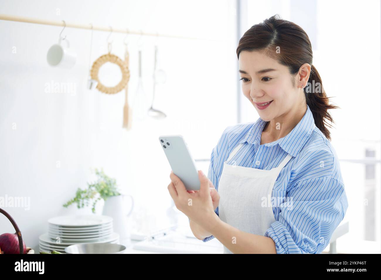 Frau, die ihr Handy ansieht, während sie in der Küche kocht Stockfoto