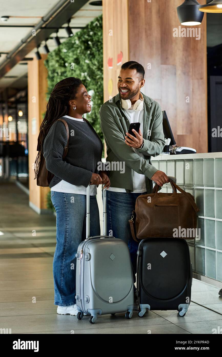 Ein fröhliches junges Paar mit Gepäck lächelt sich in einer stilvollen Hotellobby an, bereit für Abenteuer. Stockfoto