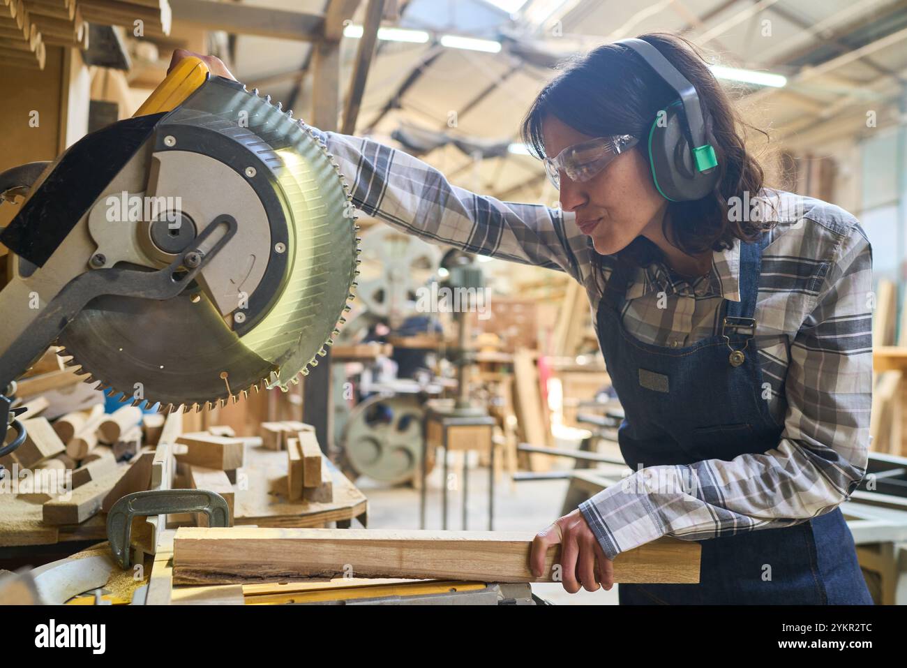 Eine fokussierte Frau arbeitet mit einer Kreissäge in einem pulsierenden Holzhof und zeigt ihre Handwerkskunst und Liebe zum Detail. Die Atmosphäre wird hervorgehoben Stockfoto