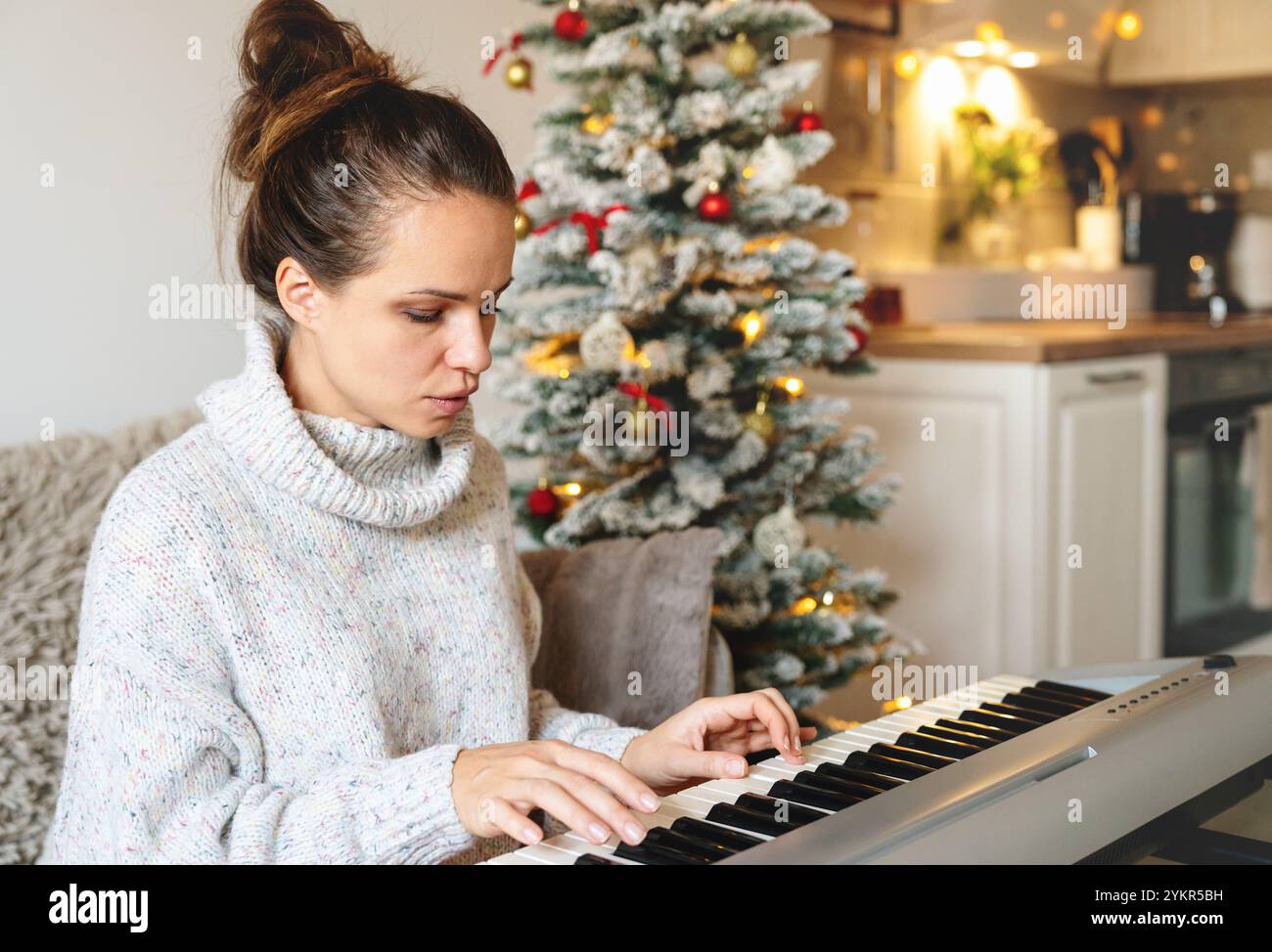 Frau im Strickpullover, die während der Weihnachtsferien elektrisches Klavier spielt. Stockfoto