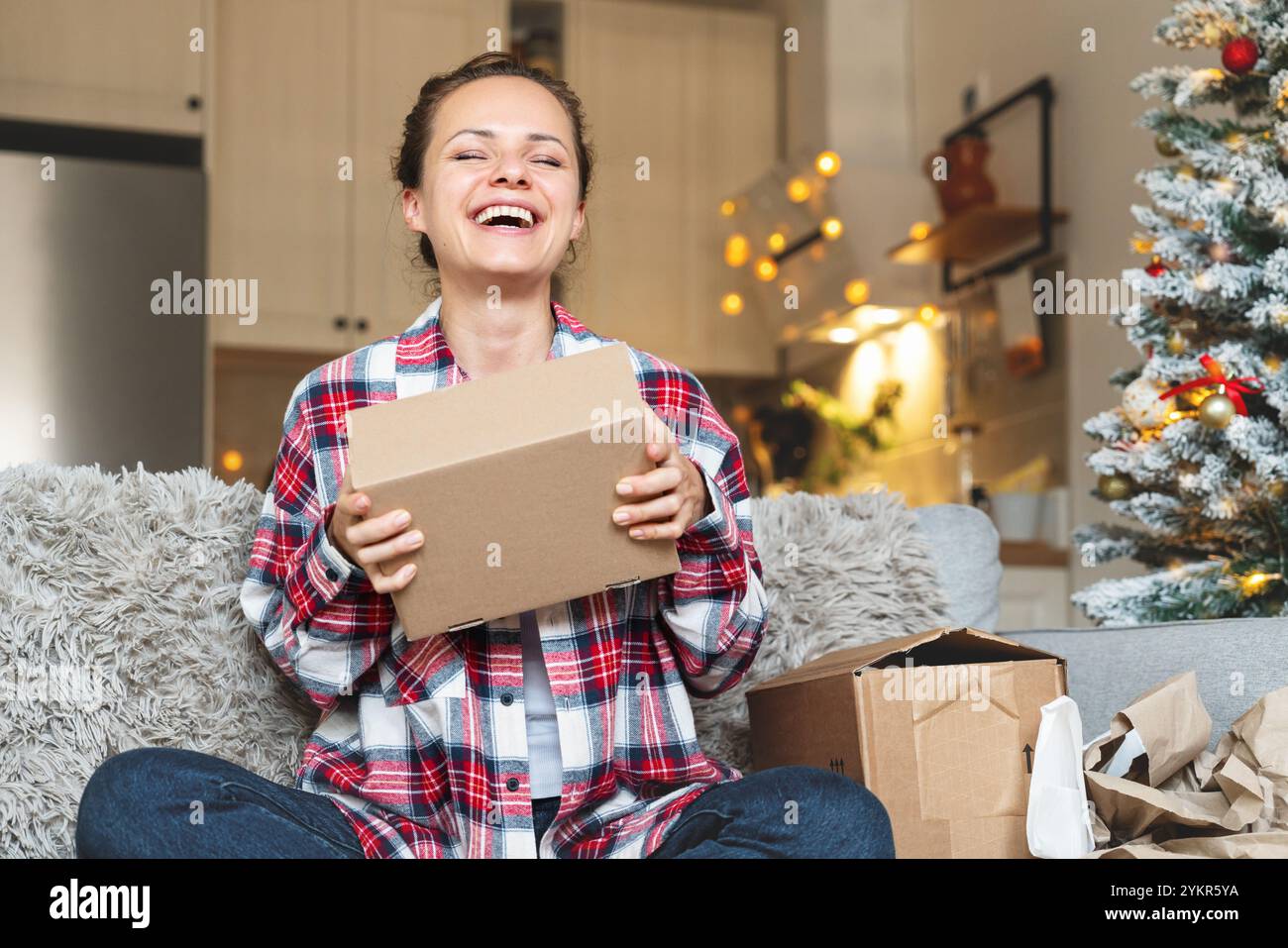 Glückliche Frau auf dem Sofa mit Lieferkarton in den Händen. Online-Shopping zu Weihnachten. Stockfoto