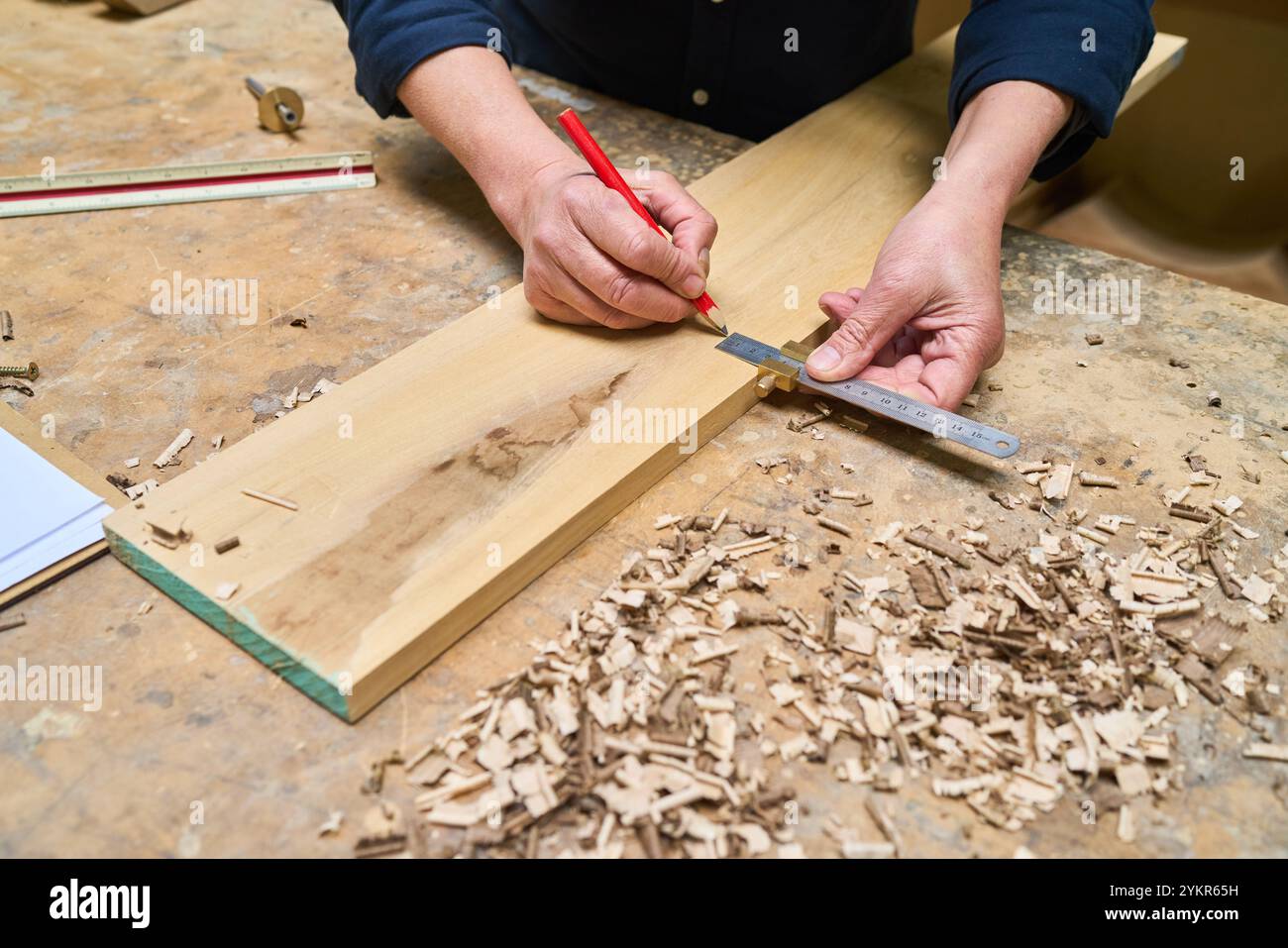 Eine Person misst in einer Holzwerkstatt mit einem Lineal und Bleistift ein Stück Holz sorgfältig und zeigt handwerkliches Können und Liebe zum Detail. Holzscha Stockfoto