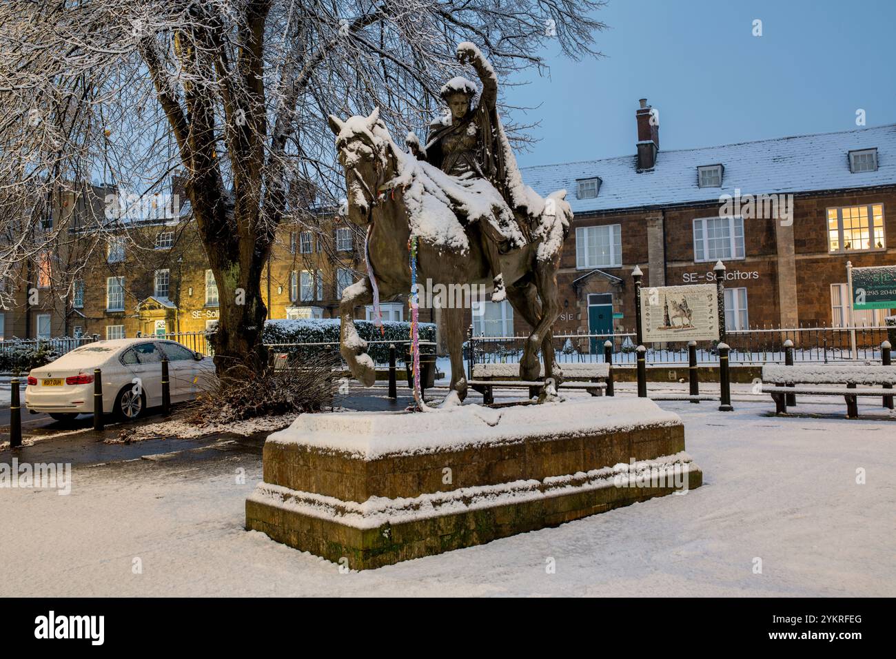 Schöne Dame Bronzestatue / Skulptur auf einem walisischen Spindelpferd neben Banbury Cross im Schnee bei Sonnenaufgang. Banbury, Oxfordshire, England Stockfoto