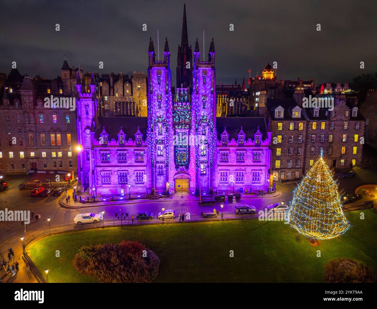 Aus der Vogelperspektive von der Drohne des New College an der Edinburgh University, beleuchtet in lila mit traditionellem Weihnachtsbaum auf dem Hügel, Edinburgh, Schottland Stockfoto