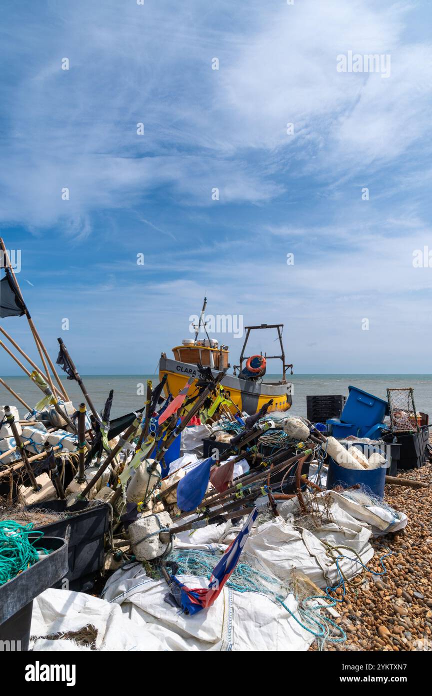 Kleines gelbes Fischerboot (Clara) hinter Anhäufungen von Angelschrott am Strand von Hastings Stockfoto