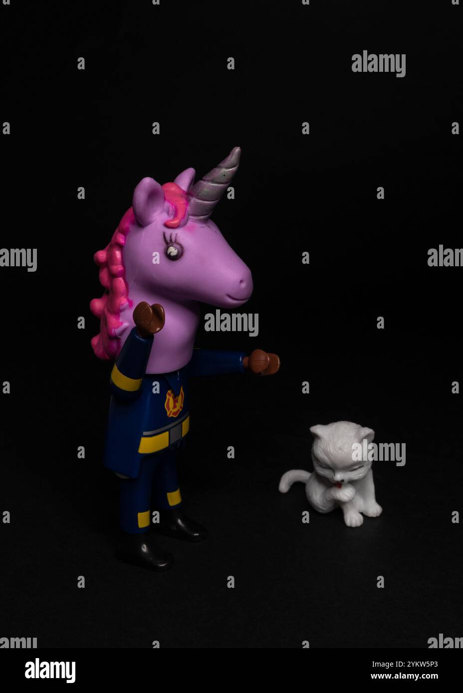 Feuerwehrfigur mit Einhornmaske, die auf eine kleine weiße Katze blickt. Ein Feuerwehrmann in Verkleidung, der ein verlorenes Kätzchen rettet. Stockfoto