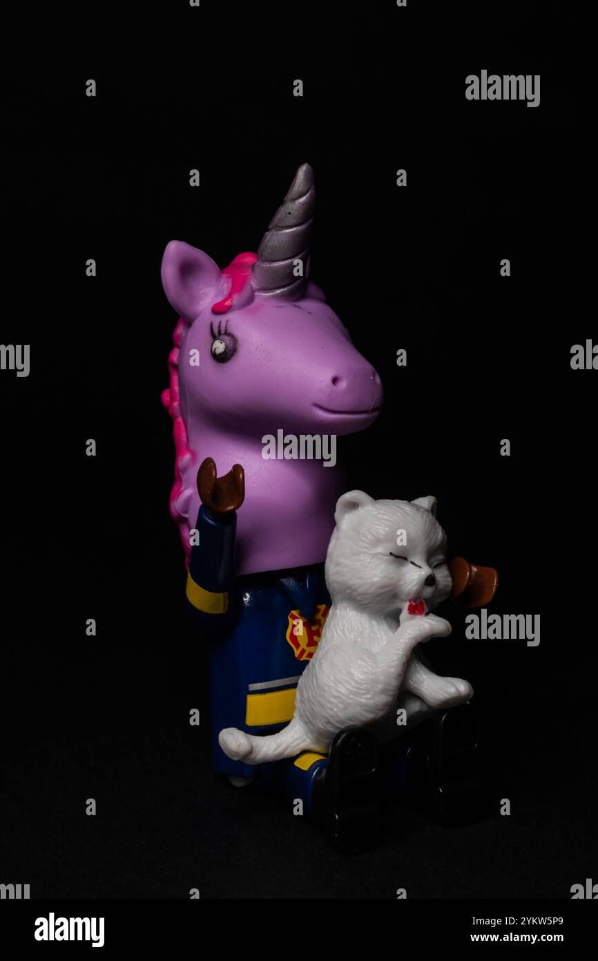 Sitzendes Feuerwehrspielzeug mit Einhornmaske und einer geretteten Katze auf seinem Schoß Stockfoto