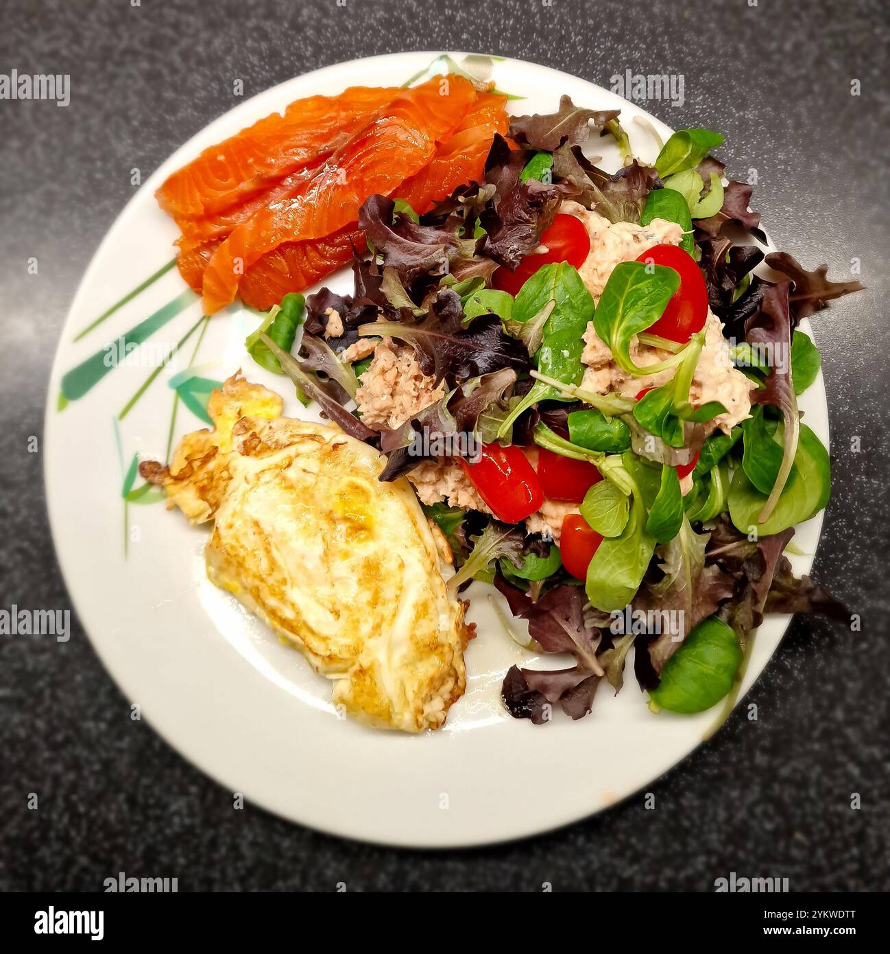 Nahaufnahme eines dekorierten Tellers mit Salat, bestehend aus verschiedenen Arten von roten und grünen Eichenblattsalaten, Lammsalat und Snacktomaten, Fisch Stockfoto
