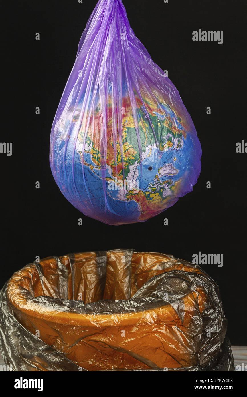 Weltkugel in Plastiktüte, die über dem Mülleimer hängt. Vertikale Aufnahme isoliert auf Schwarz Stockfoto