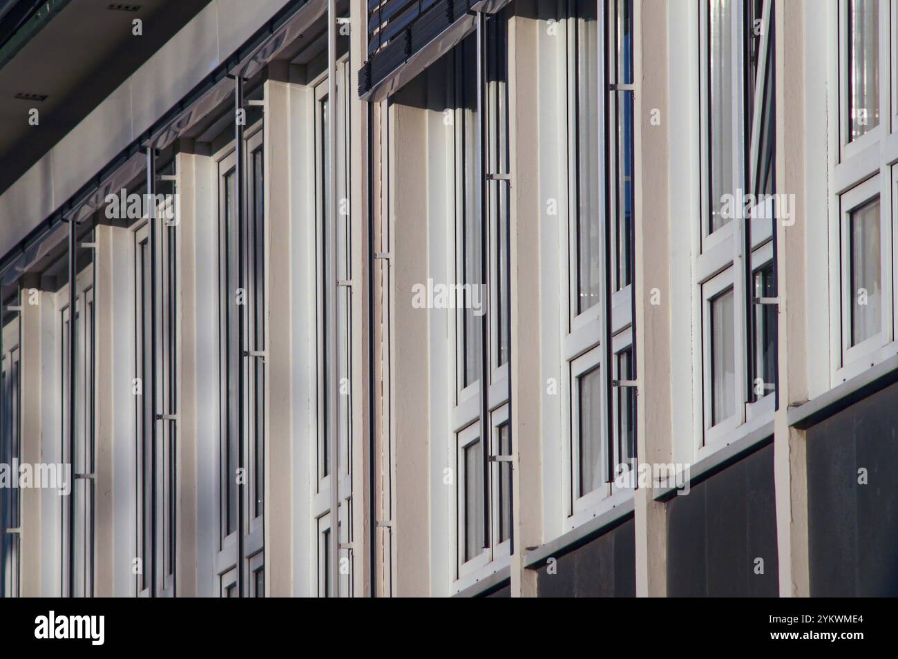 Weiße Fensterrahmen mit Außenjalousien erzeugen ein rhythmisches Muster auf einer modernen Gebäudefassade, das zeitgenössisches architektonisches Design zeigt Stockfoto