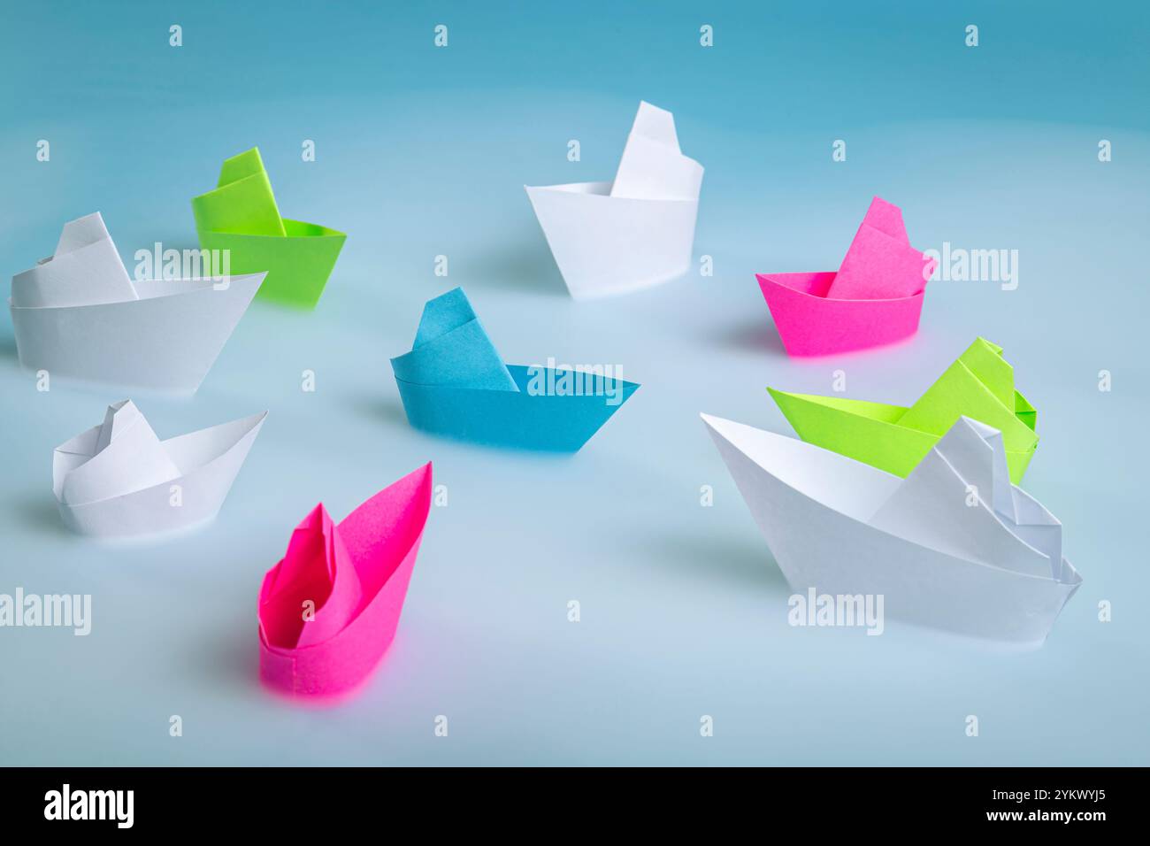 Gruppe von mehrfarbigen Booten um ein blaues Boot auf einem blauen nebeligen Hintergrund, das das Meer symbolisiert. Führungskonzept. Stockfoto