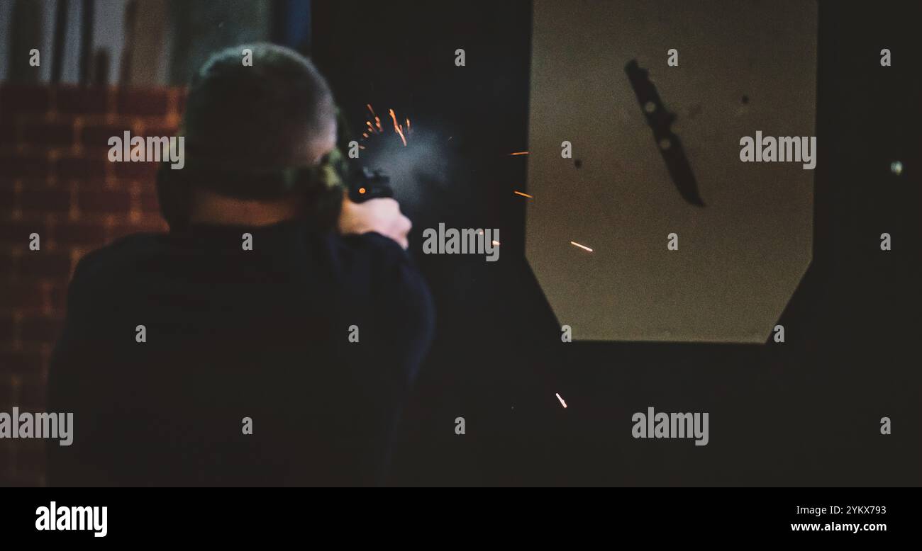 Das Bild zeigt einen Mann auf einem Schießstand. Der Mann wird von hinten gesehen und feuert eine Handfeuerwaffe ab. Sichtbare Funken und Rauch kommen aus der Waffe. Stockfoto