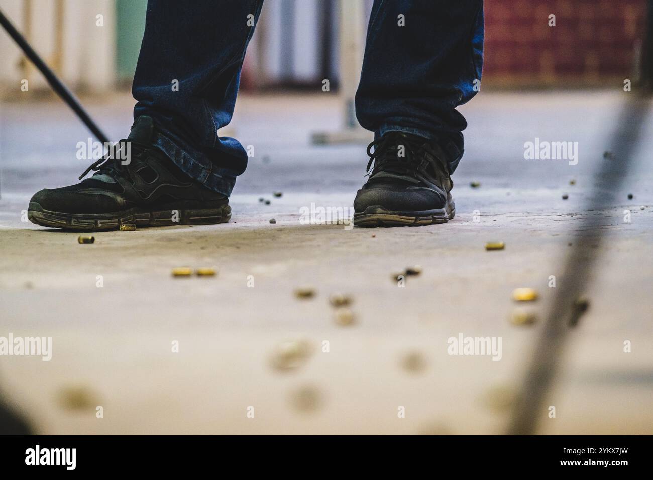 Nahaufnahme der Füße einer Person. Die Person trägt schwarze Schuhe und dunkle Hosen. Der Boden scheint mit einer verschwendeten Kugel bedeckt zu sein Stockfoto