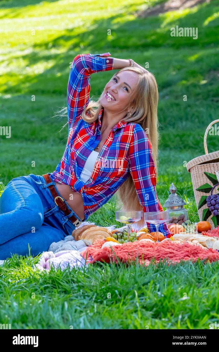 Ein atemberaubendes europäisches Model, gekleidet in gemütlichen Herbstschichten, genießt an einem frischen Herbsttag ein malerisches Picknick im Freien. Goldene Blätter umgeben sie während sie Stockfoto