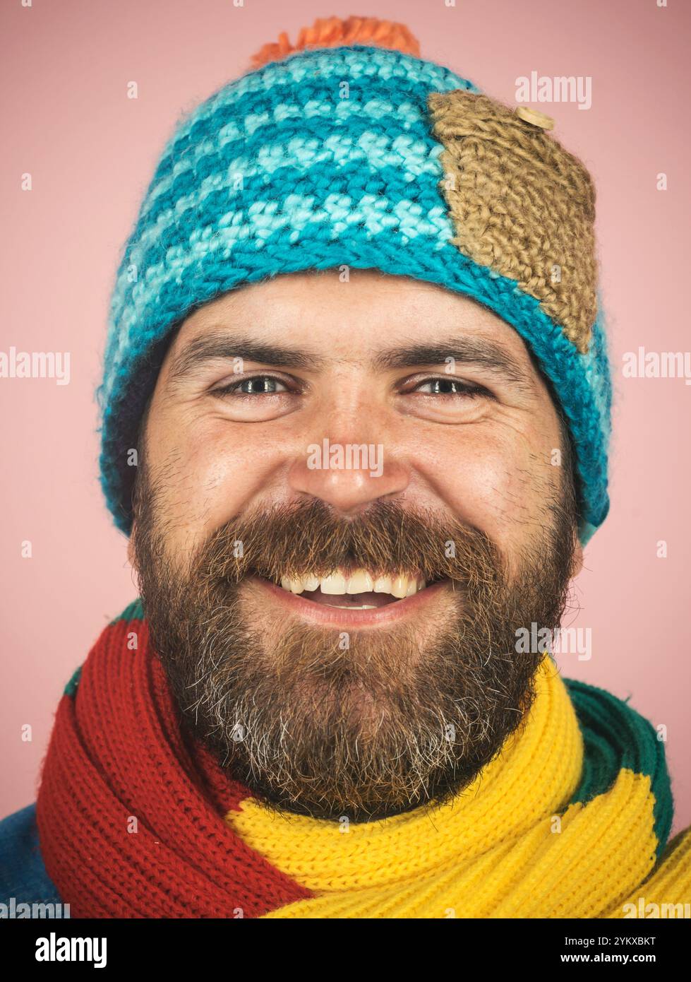 Nahaufnahme Porträt eines lächelnden bärtigen Mannes in buntem Schal und Strickmütze. Modischer Mann in Winterkleidung. Lässige Wintermode für Herren. Gut Aussehend Stockfoto