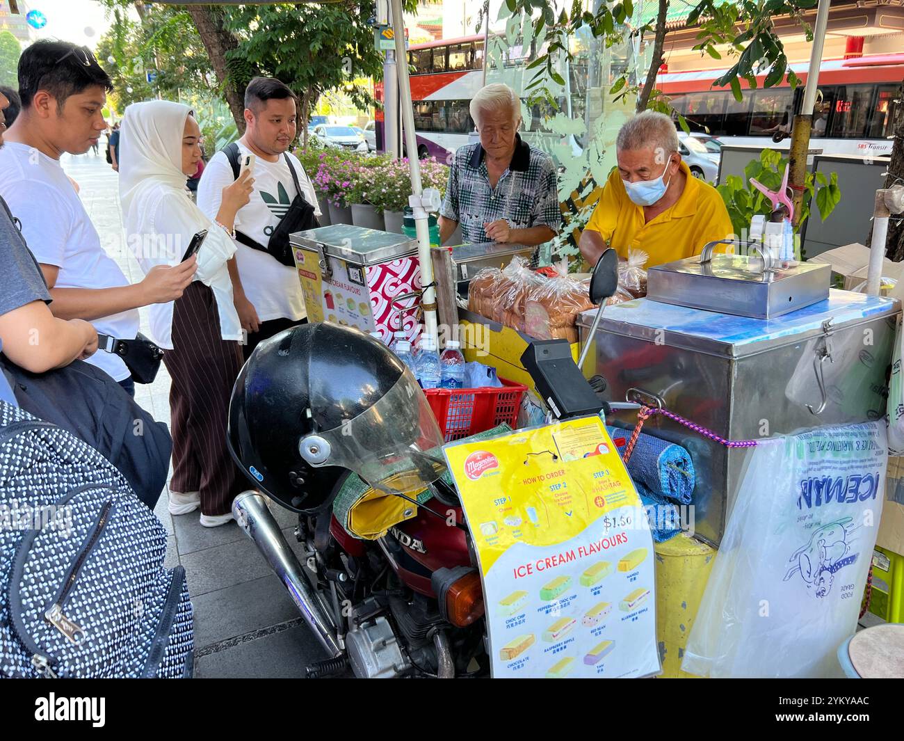 Mobiler Eisverkäufer auf der Straße in der Orchard Road, einem beliebten Dessert-Ort für Touristen, indonesische Dame, die Fotos von den 2 Männern macht. Singapur. Stockfoto