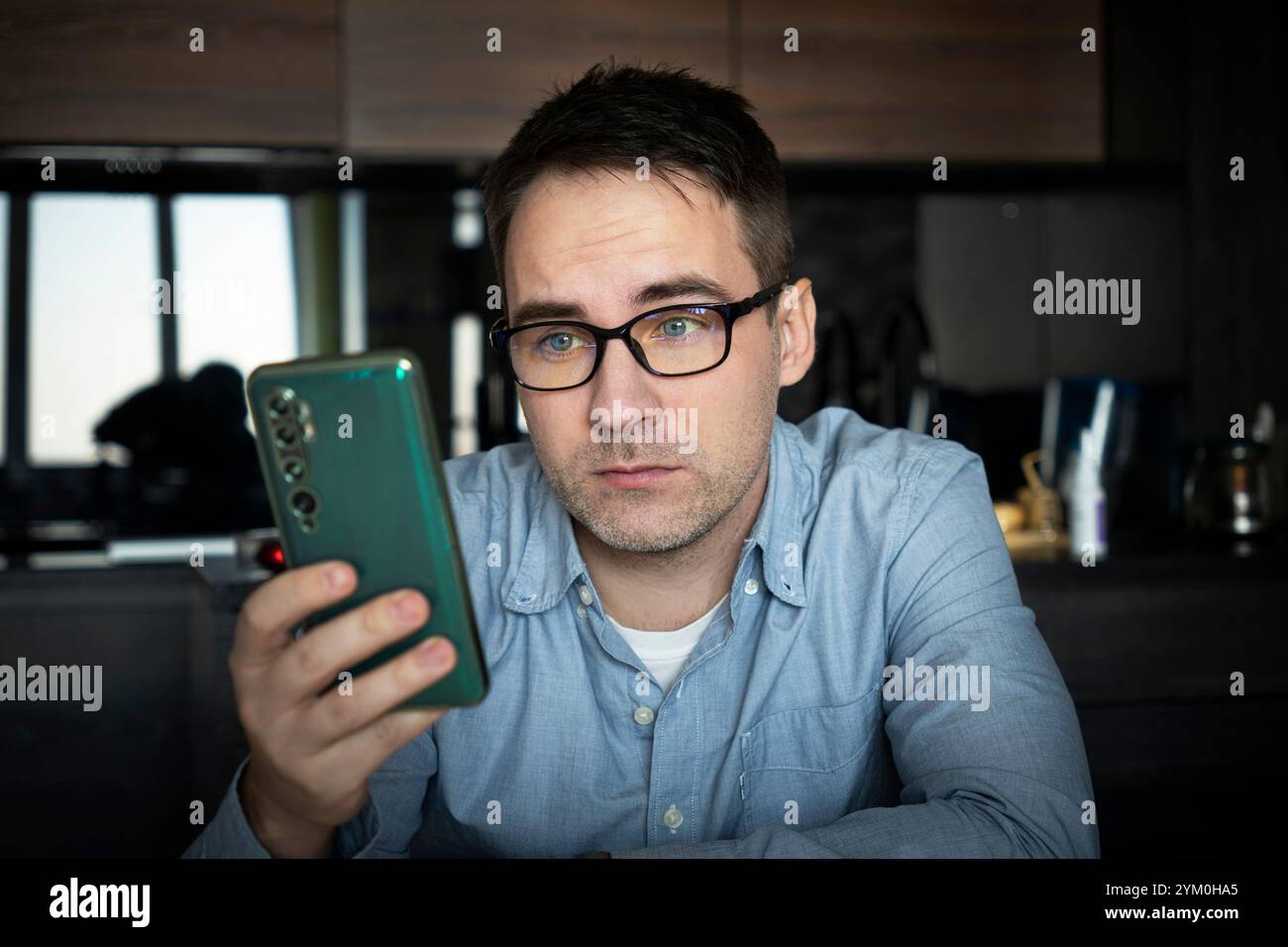 Männchen benutzen moderne Handygeräte, Texten oder Messaging über WLAN. Ein weißer Mann mit Brille sitzt am Schreibtisch im Heimbüro. Schauen Sie sich das Smartphone sc an Stockfoto