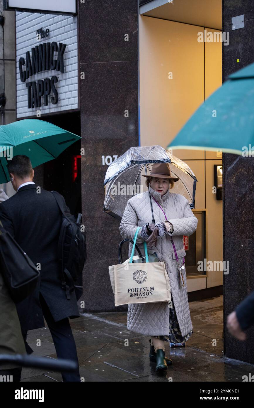 Eine gut gekleidete City Lady macht sich auf den Weg entlang der Cannon Street mit einer Fortnum & Mason Tasche an Stadtarbeitern in der City of London, England, Großbritannien Stockfoto Eine gut gekleidete City Lady macht sich auf den Weg entlang der Cannon Street mit einer Fortnum & Mason Tasche an Stadtarbeitern in der City of London, England, Großbritannien Stockfoto