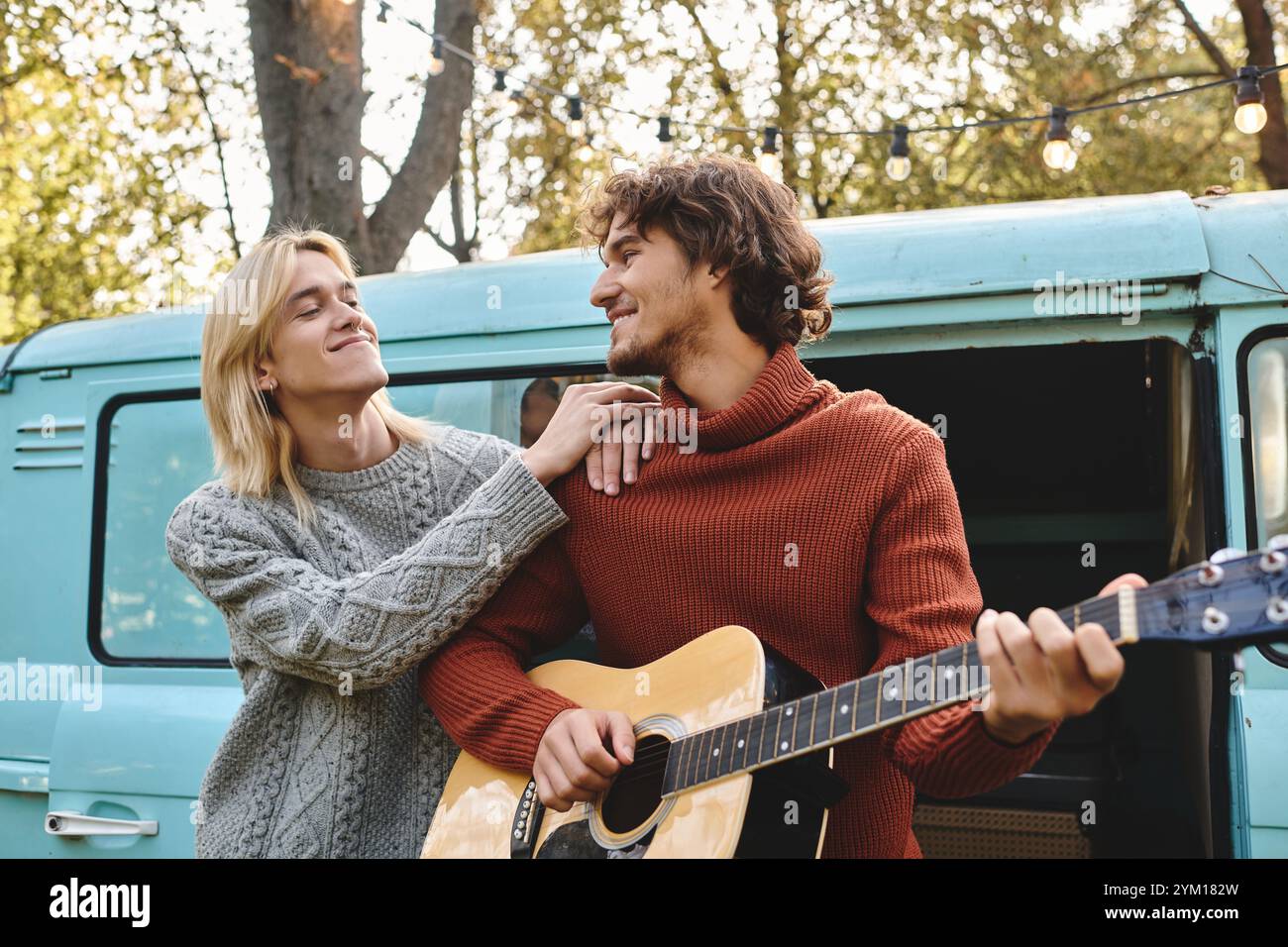 Zwei junge und gutaussehende Menschen teilen einen freudigen Moment, während einer Gitarre spielt und der andere liebevoll schaut. Umgeben von der Natur strahlen sie Wärme aus Stockfoto