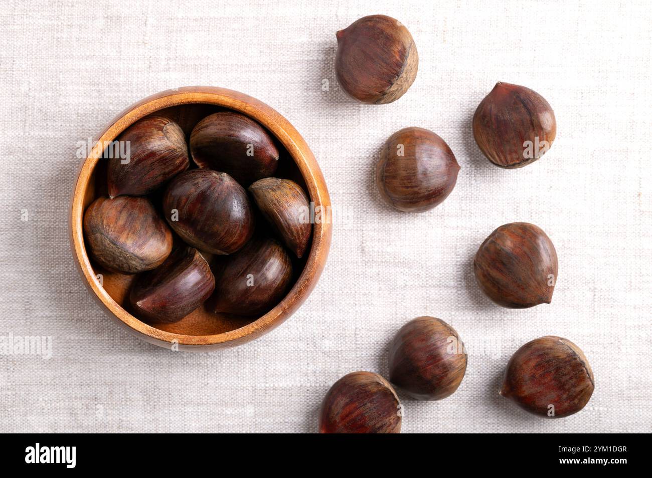 Süße Kastanien in einer Holzschale auf Leinen. Roh, ganz und ungeschälte Castanea sativa, kann roh, kandiert, gekocht, zu Mehl gemahlen usw. gegessen werden Stockfoto