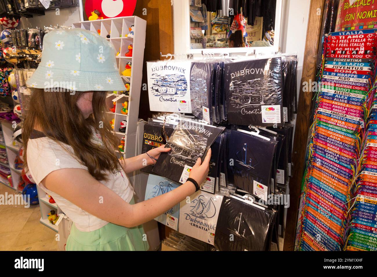Kinder im Alter von 12 Jahren / Kinder / Mädchen, die T-Shirts in einem Souvenirladen für Touristen stöbern und Souvenirs aus Zimmern innerhalb der Stadtmauer / Stadtmauern verkaufen; Altstadt von Dubrovnik, Kroatien. (138) Stockfoto