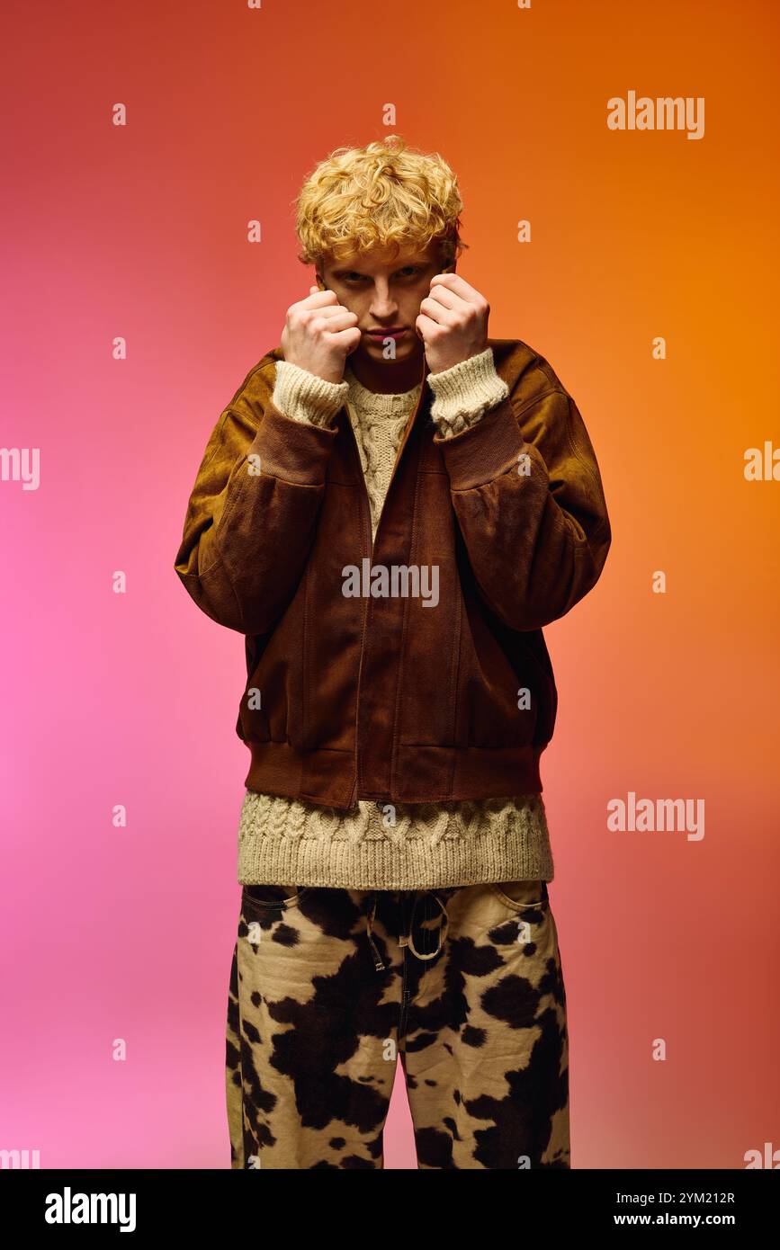 Ein Mann steht selbstbewusst vor einer lebhaften Kulisse aus Rosa- und Orangetönen und präsentiert ein stilvolles Winteroutfit, das perfekt für die Weihnachtszeit ist. Stockfoto